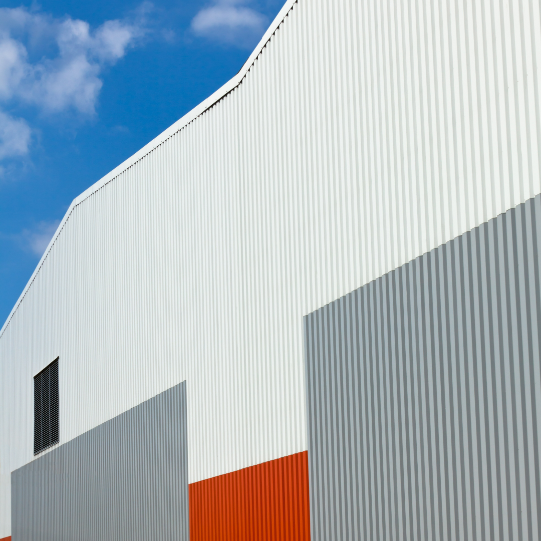 Custom Trim Excellence Modern architectural building with white, gray, and orange corrugated panels under a clear blue sky.